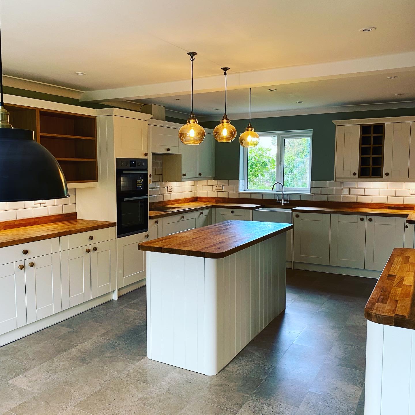 Cream shaker kitchen with oak worktops, an island and three glass pendant lights